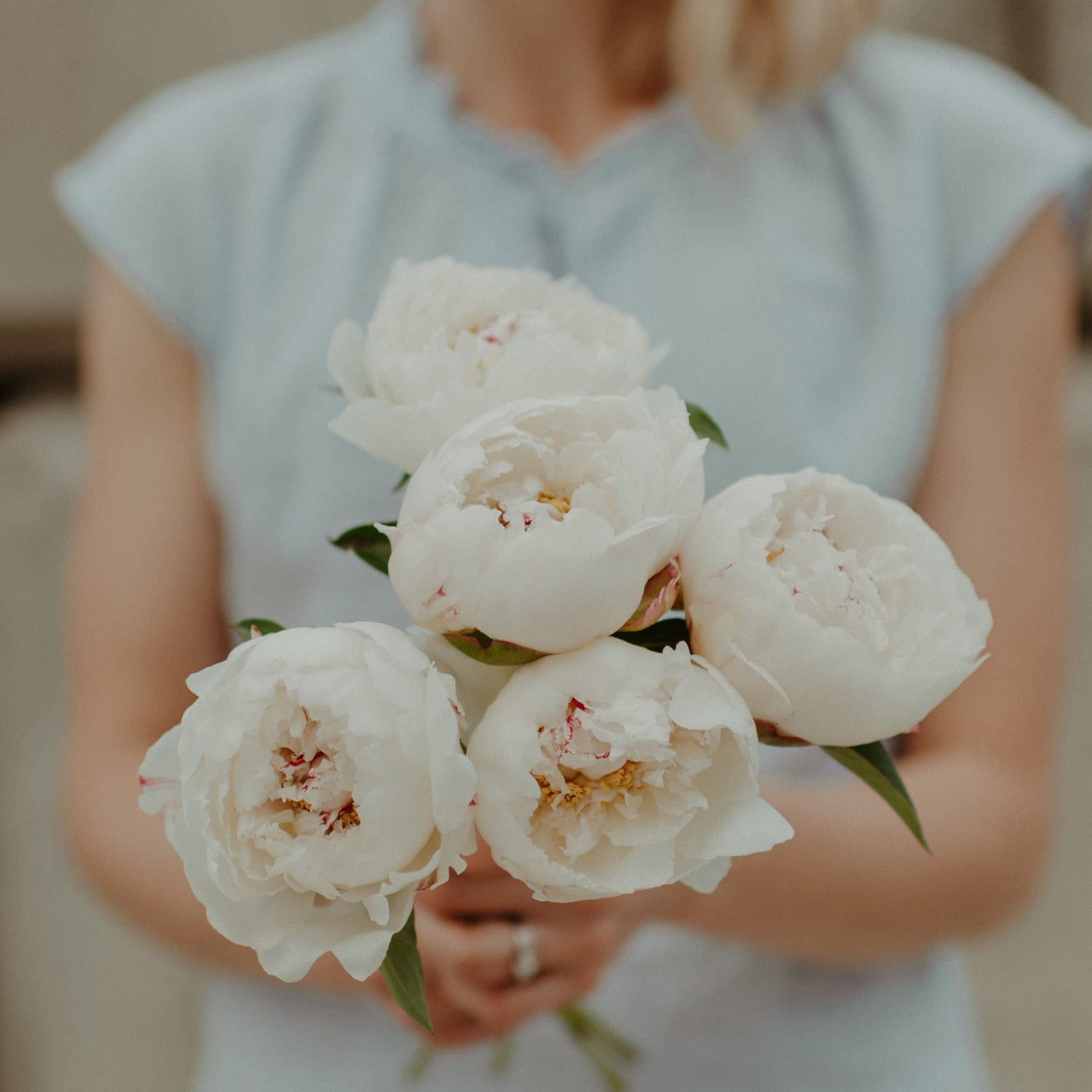Woman holding a bouquet of white peony flowers with a blurred background